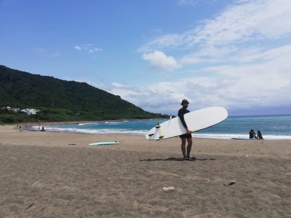 homme portant une planche de surf sur une plage a taiwan
